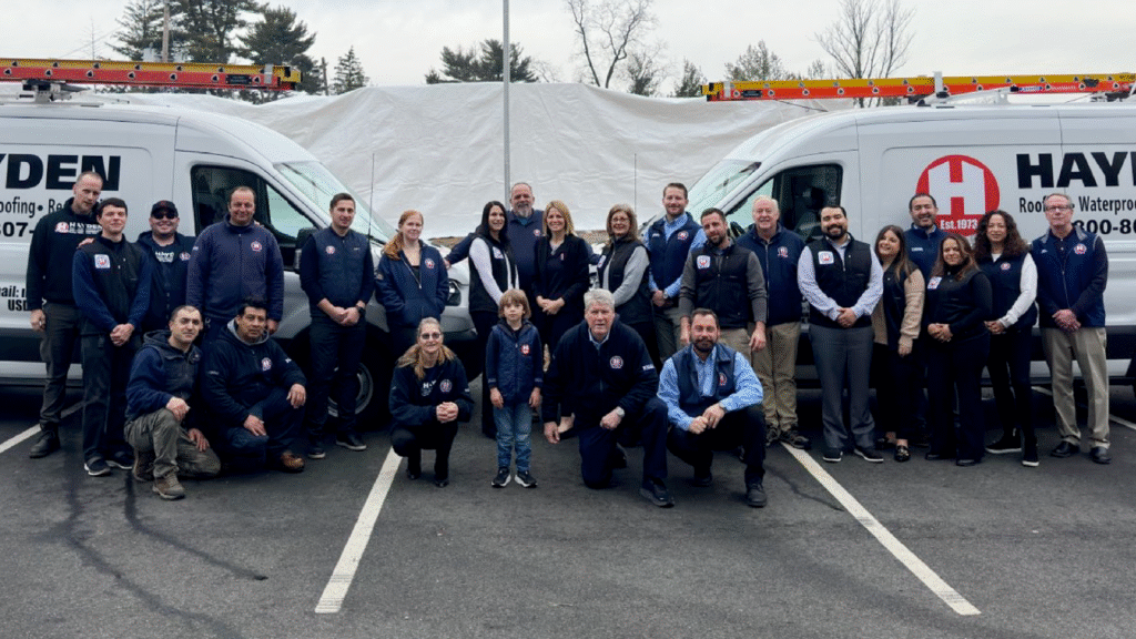 Hayden Building Maintenance Corp. team of roofing and waterproofing professionals standing together in front of company service vans.